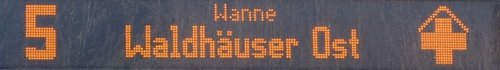 Eine digitale Anzeige zeigt die Zahl 5 und den Text "Waldhäuser Ost" in orangefarbenen LED-Pixeln. Neben dem Text ist ein Symbol, das eine Art Haus oder Gebäude darstellt.