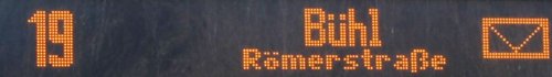 Eine digitale Anzeige zeigt die Zahl 19 und den Namen "Bühl" sowie die Straße "Römerstraße". Rechts ist ein kleines Symbol, das wie ein Briefumschlag aussieht.